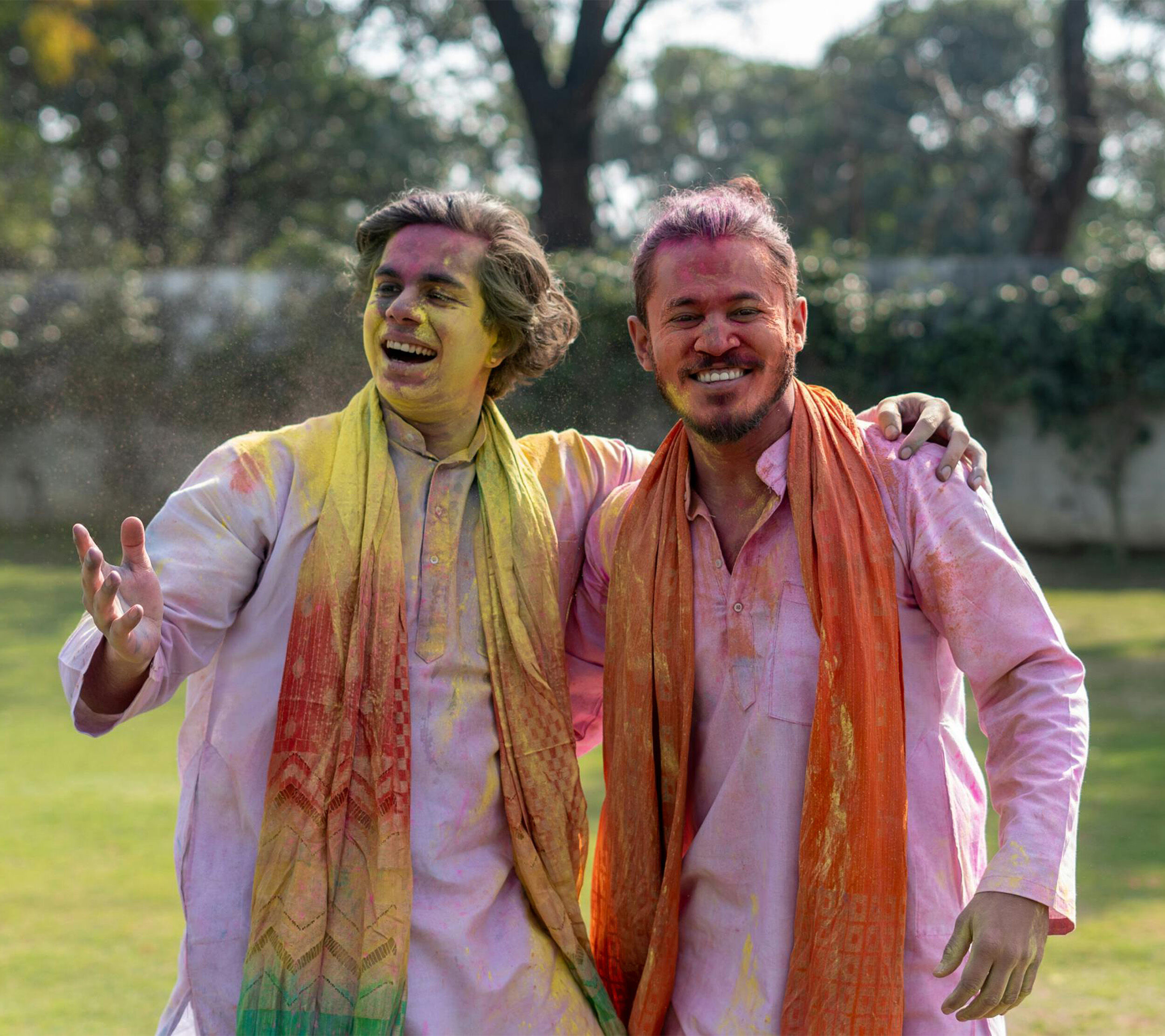Two men covered in colorful powder celebrating Holi outdoors.